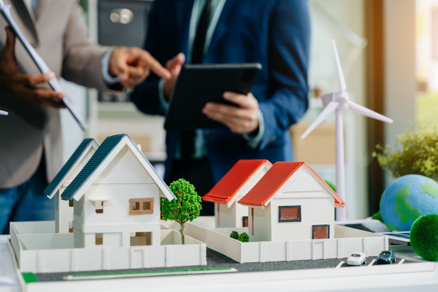 Real estate agents reviewing houses for sale with miniature home models and a tablet in a modern office setting