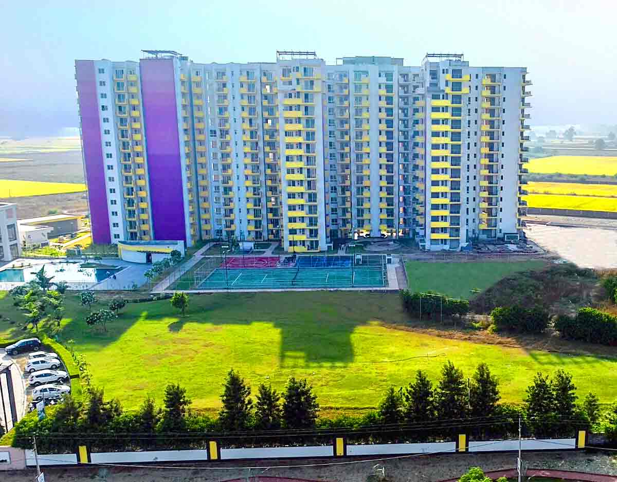An aerial eye-level shot captures a modern multi-story apartment complex under a bright, clear sky.