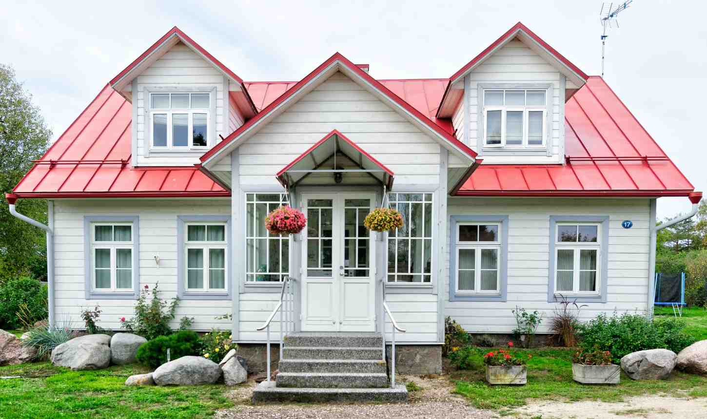 Modern white wooden house with a red metal roof and blooming flower baskets.
